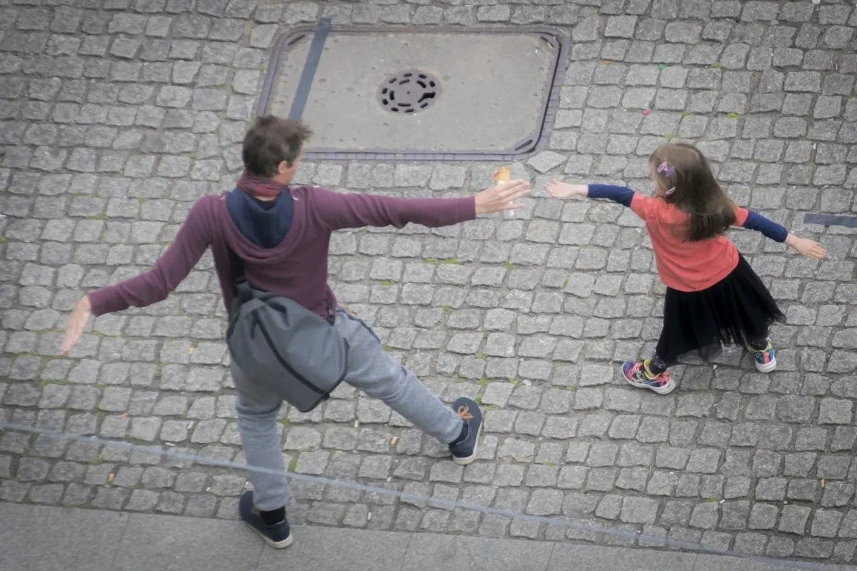 Adult and child mirroring each other with outstretched arms on cobblestones